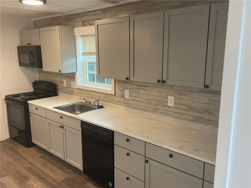 Kitchen featuring black appliances, decorative backsplash, gray cabinetry, and dark wood-style flooring