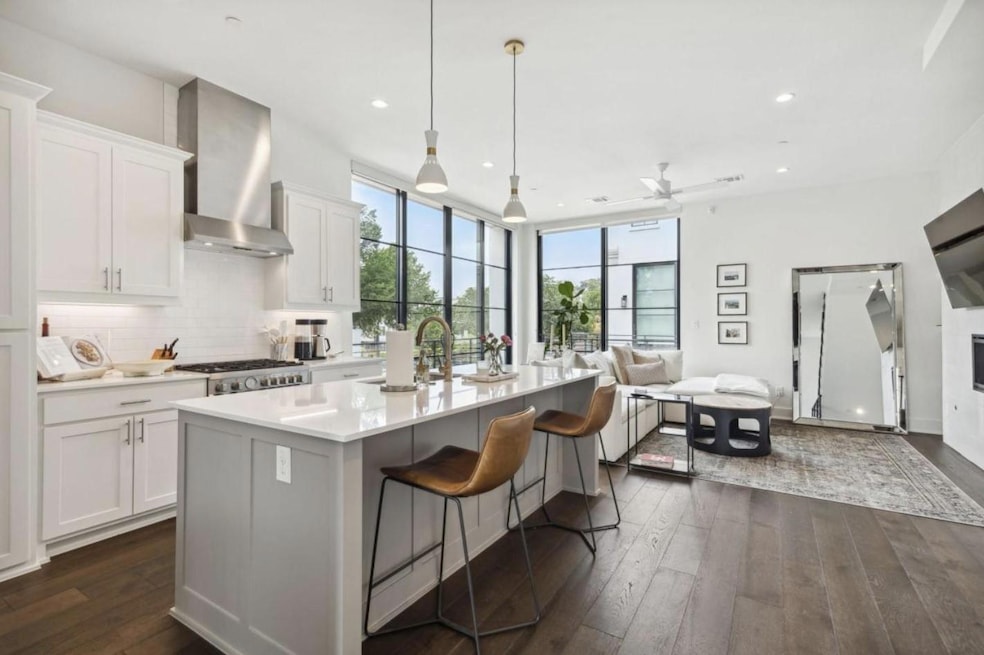 Kitchen featuring decorative light fixtures, a center island with sink, dark wood-type flooring, wall chimney exhaust hood, and white cabinetry