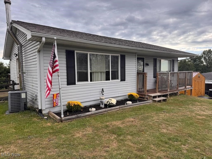 View of front of house with a storage shed, a front yard, a wooden deck, and roof with shingles