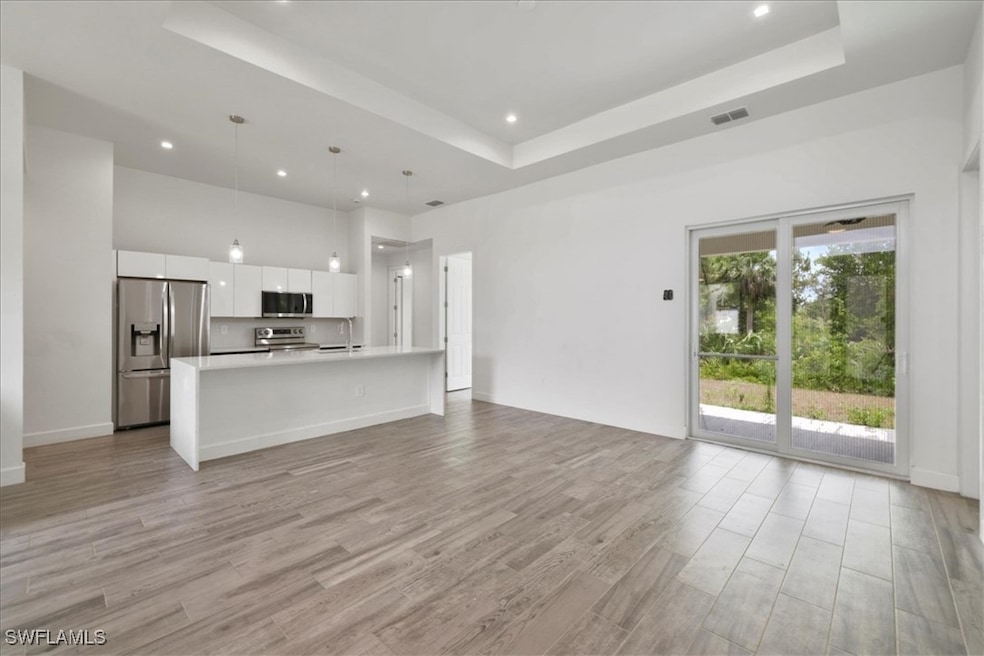 Unfurnished living room with a tray ceiling, light wood-style floors, recessed lighting, and a towering ceiling