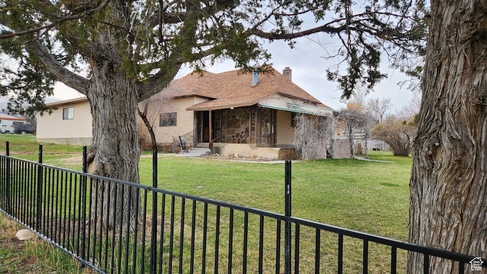 View of front of house from the corner with a front yard, stone siding, roof with shingles, a chimney, and fence