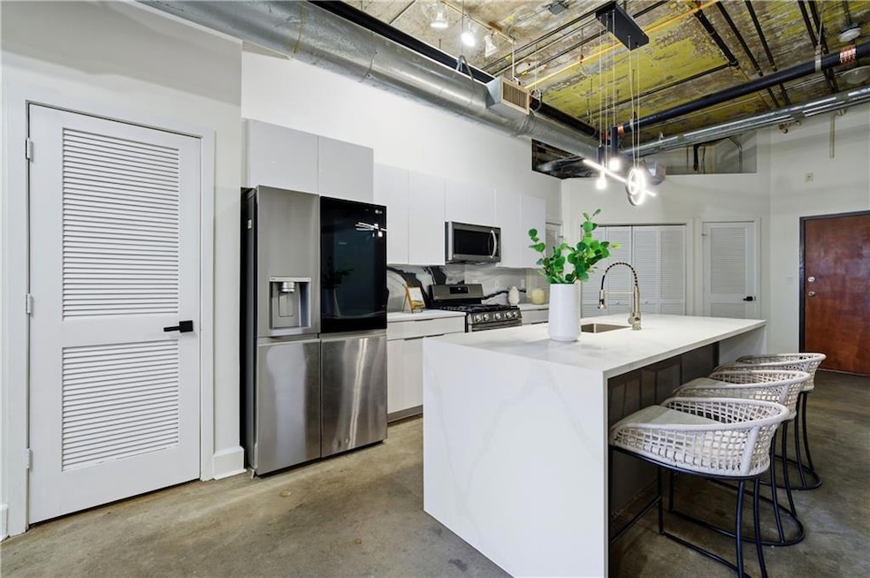 Kitchen with stainless steel appliances, hanging light fixtures, concrete flooring, a towering ceiling, and a breakfast bar area