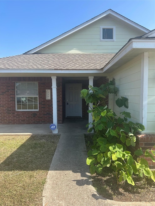 View of exterior entry with a shingled roof, brick siding, and a porch
