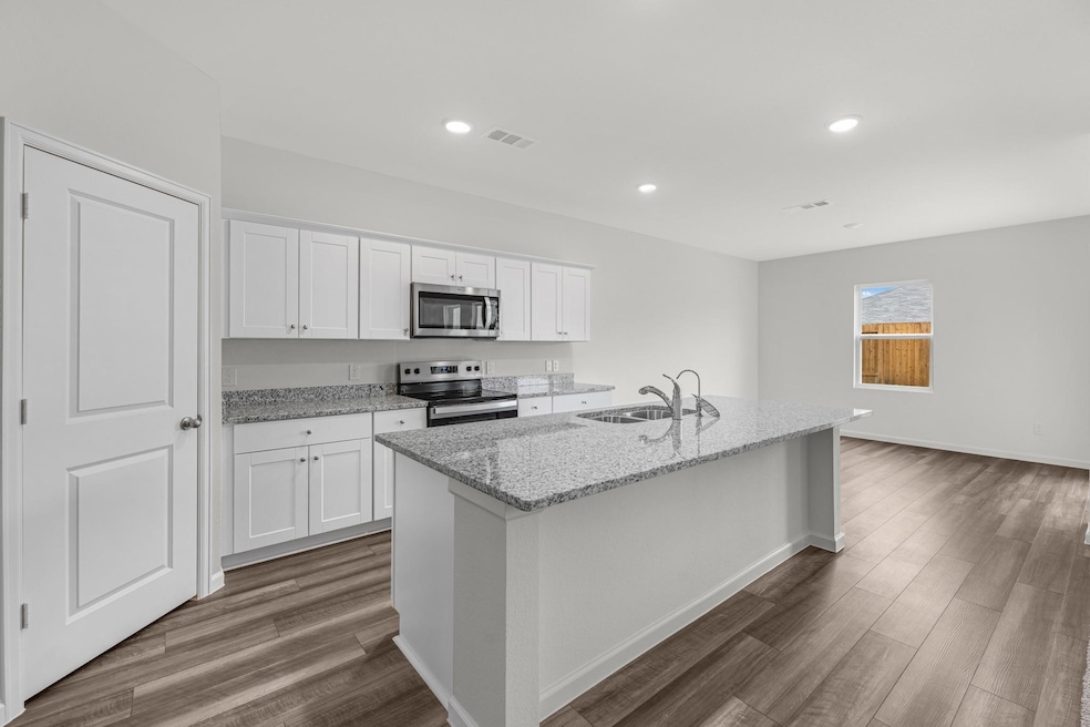 Kitchen featuring white cabinets, light stone counters, stainless steel appliances, a kitchen island with sink, and recessed lighting