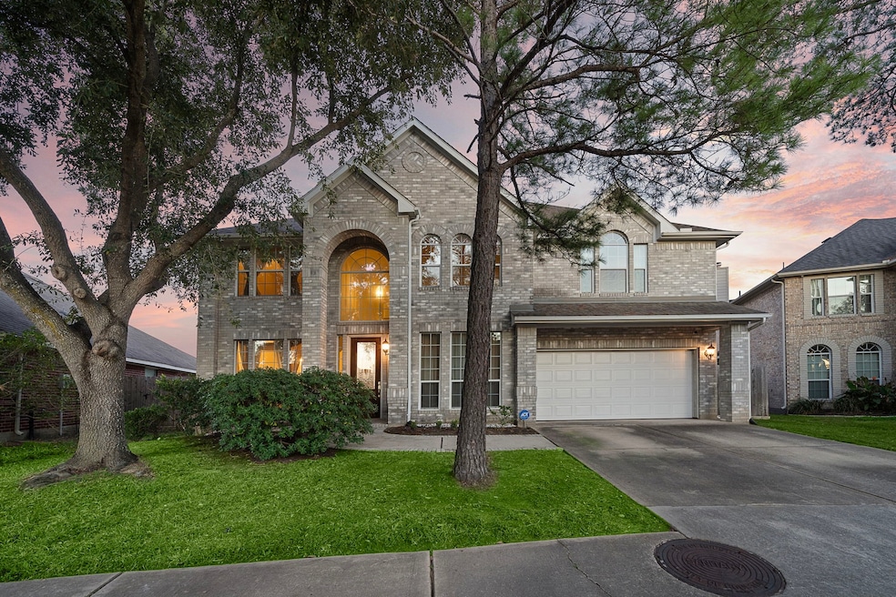 Two-story brick home with arched entryway and attached garage, flanked by mature trees.