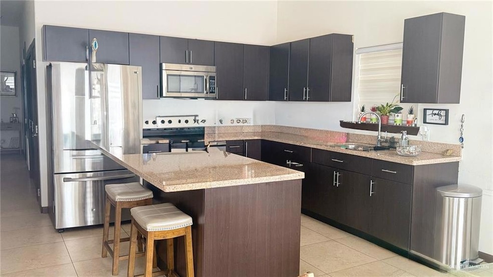 Kitchen with appliances with stainless steel finishes, light tile patterned floors, a kitchen island, and a kitchen bar