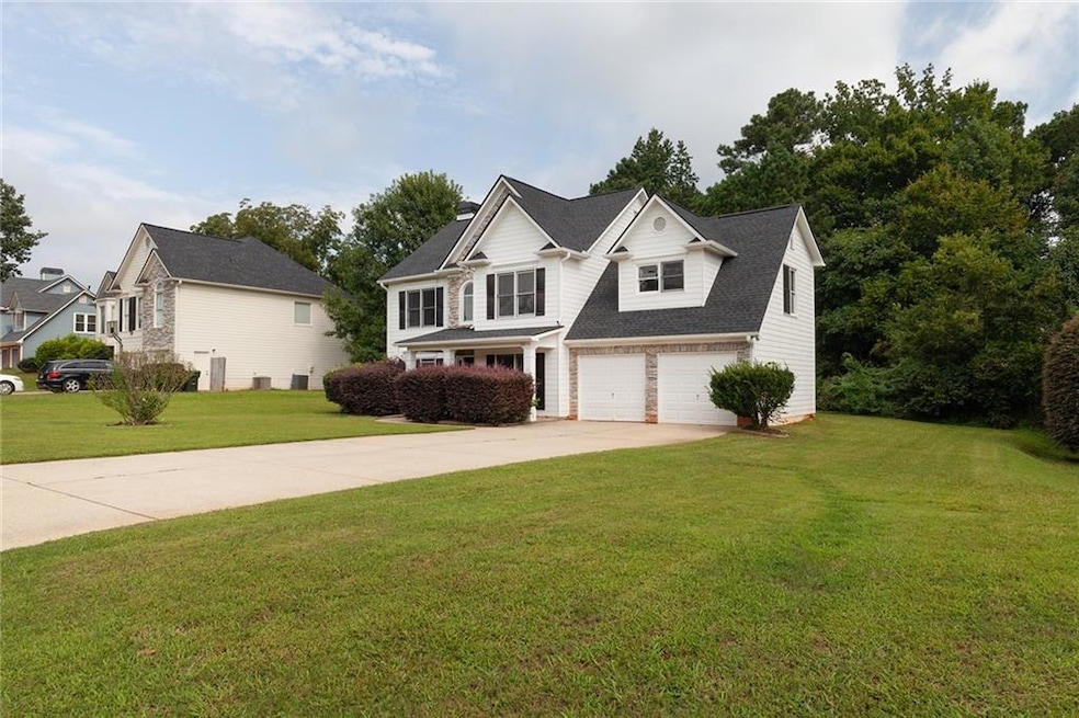 Traditional-style home with a front yard, concrete driveway, a garage, a shingled roof, and stone siding