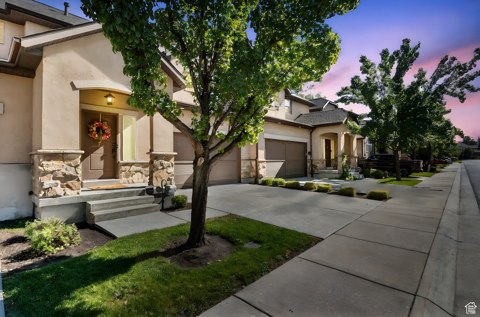 View of front of home featuring driveway, stucco siding, a garage, and stone siding