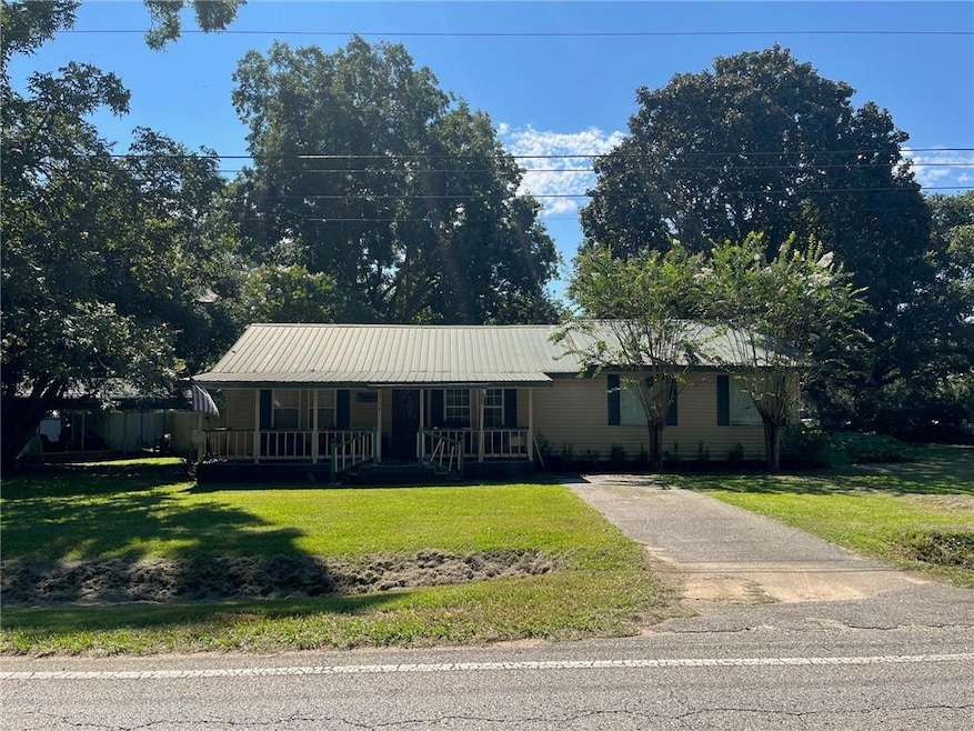 Ranch-style house featuring a porch, a front lawn, a metal roof, and driveway