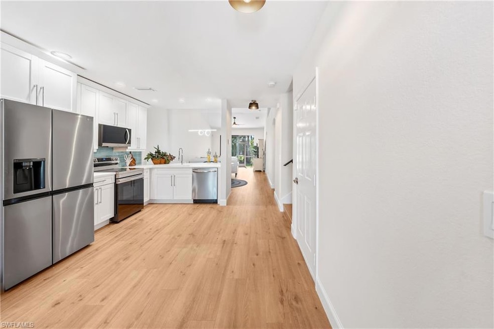 Kitchen featuring stainless steel appliances, tasteful backsplash, light wood-type flooring, white cabinetry, and light countertops