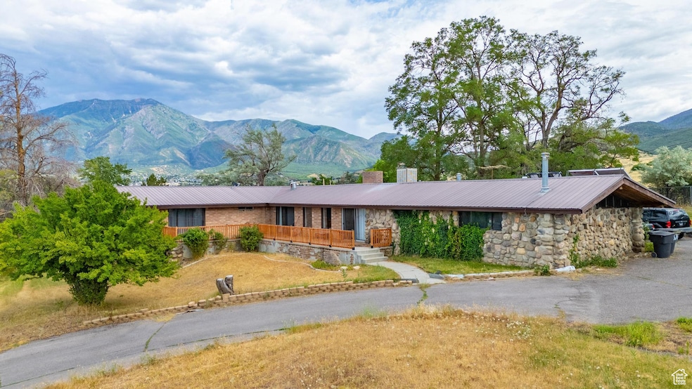 View of front of house featuring a mountain view, stone siding, a metal roof, a chimney, and driveway