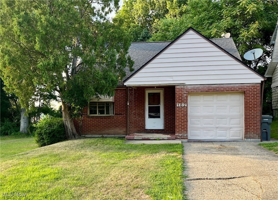 View of front of property featuring driveway, a front yard, brick siding, roof with shingles, and an attached garage