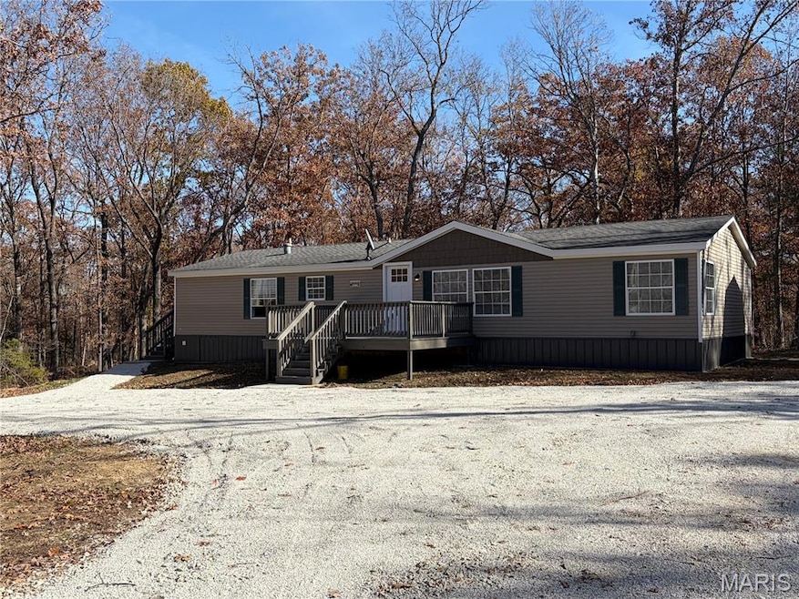 Manufactured / mobile home featuring a deck, stairway, gravel driveway, and a shingled roof