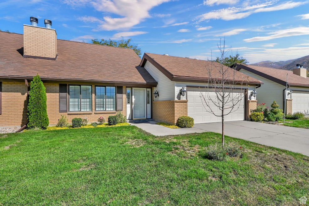 View of front of home with brick siding, concrete driveway, a front yard, an attached garage, and a chimney