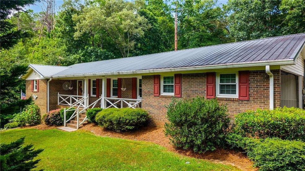 Single story home with a porch, brick siding, a front lawn, and a metal roof