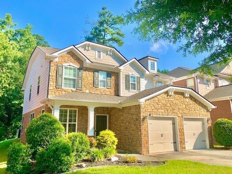 Craftsman-style home with an attached garage, stone siding, driveway, and roof with shingles