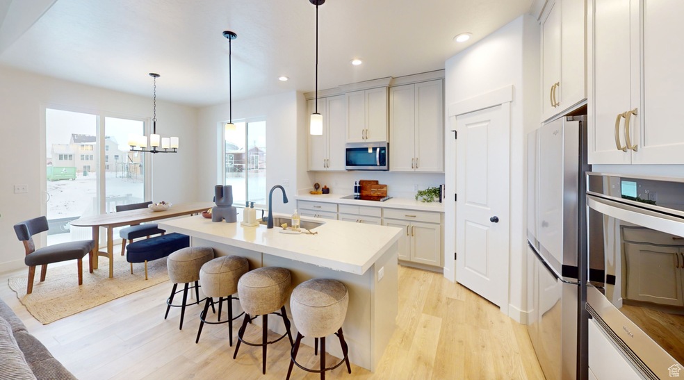 Kitchen with stainless steel appliances, a sink, light wood-style flooring, a breakfast bar, and an island with sink