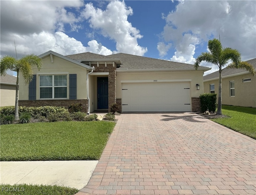 View of front facade with a front yard, decorative driveway, stucco siding, and an attached garage