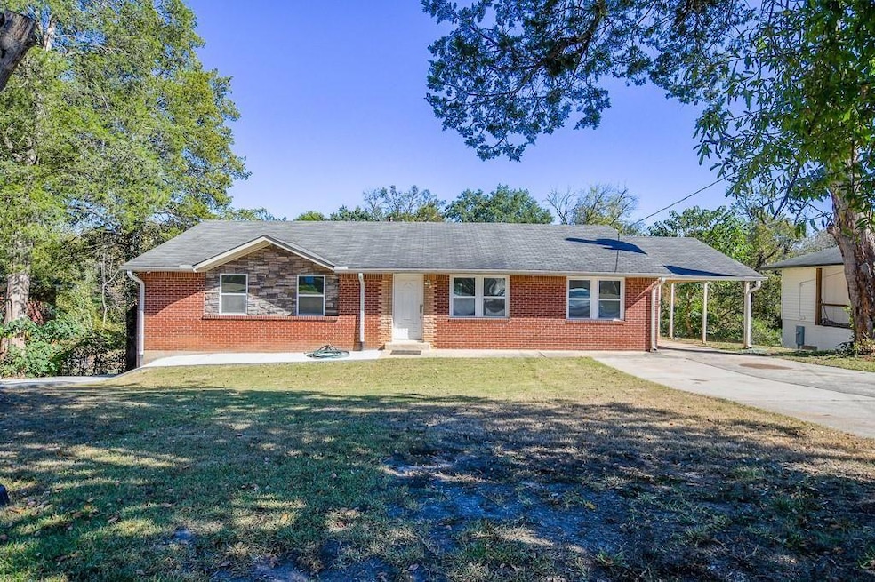 Single story home featuring a front lawn, driveway, brick siding, a shingled roof, and an attached carport