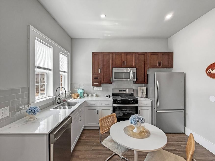 Kitchen with dark wood-style floors, appliances with stainless steel finishes, decorative backsplash, and recessed lighting