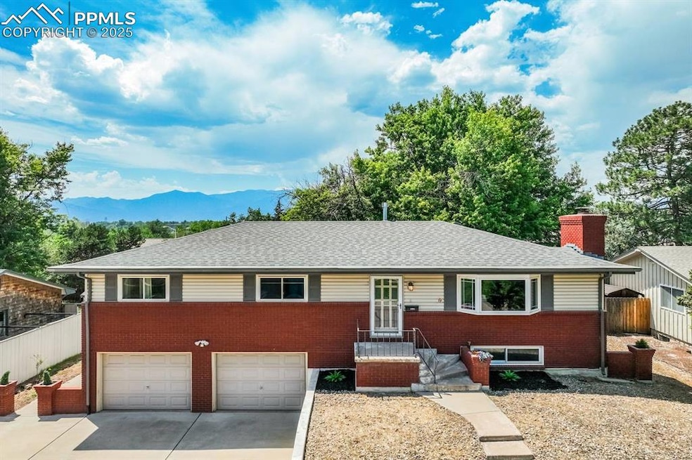 Single story home with concrete driveway, a mountain view, brick siding, an attached garage, and a chimney