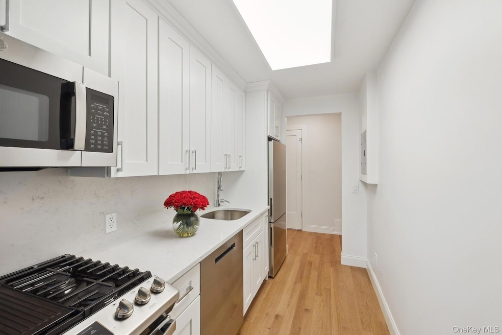 Kitchen with white cabinetry, appliances with stainless steel finishes, light wood-style flooring, light stone countertops, and decorative backsplash