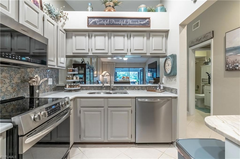 Kitchen featuring stainless steel appliances, light tile patterned floors, light countertops, tasteful backsplash, and gray cabinets