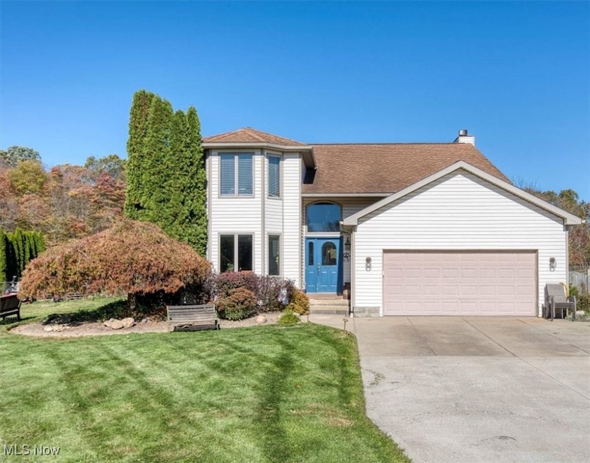 Traditional-style home featuring a front yard, a chimney, driveway, and an attached garage