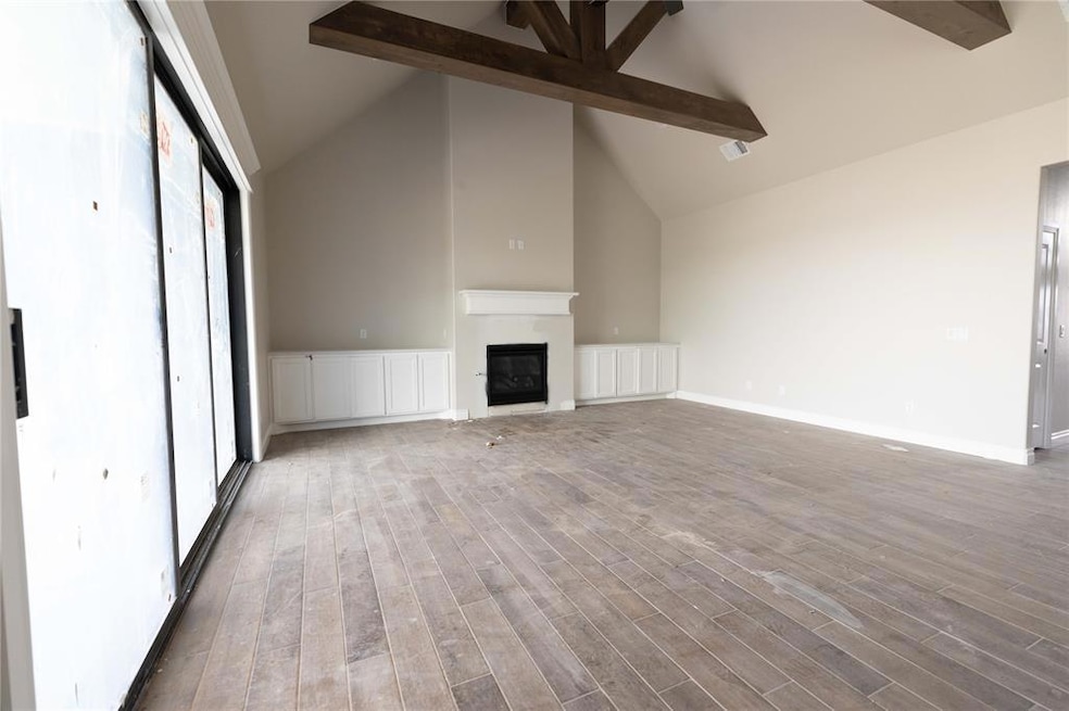 Unfurnished living room featuring beam ceiling, a glass covered fireplace, wood finished floors, high vaulted ceiling, and baseboards