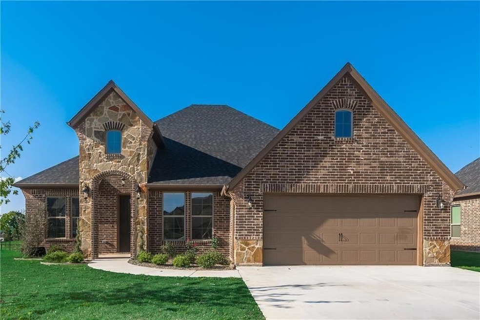 View of front facade with driveway, stone siding, brick siding, and roof with shingles