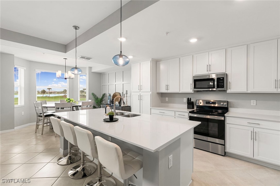 Kitchen with stainless steel appliances, light tile patterned flooring, decorative light fixtures, a breakfast bar, and white cabinetry