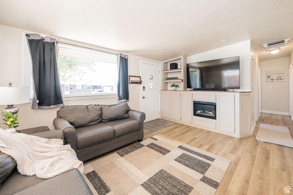 Living area featuring a textured ceiling, light wood-type flooring, and a glass covered fireplace