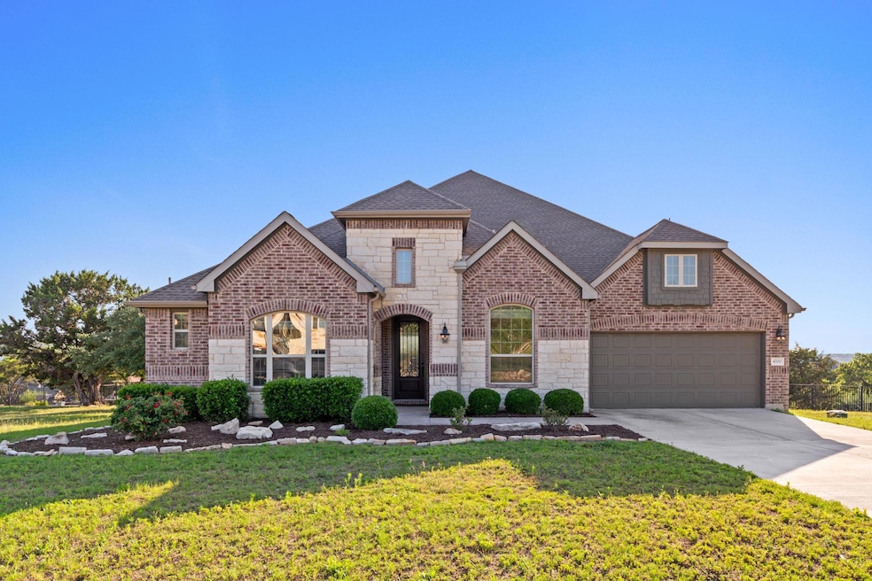 French provincial home featuring driveway, stone siding, a front yard, brick siding, and roof with shingles