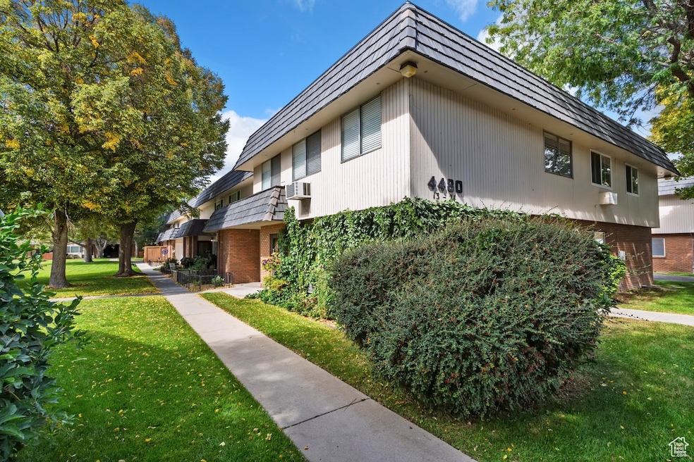 View of side of home featuring mansard roof, a yard, brick siding, and a balcony