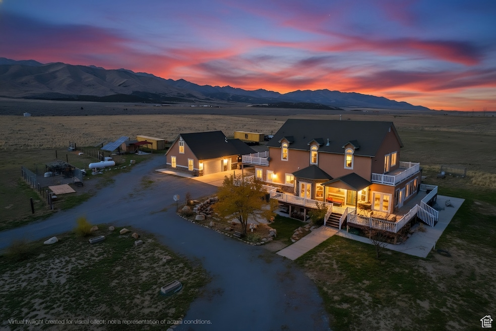 South side of house at dusk featuring driveway, a balcony, a deck with mountain view, and a yard.