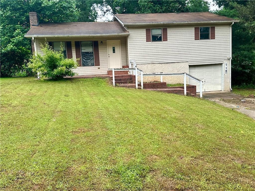 Tri-level home featuring an attached garage, a chimney, driveway, and a front yard