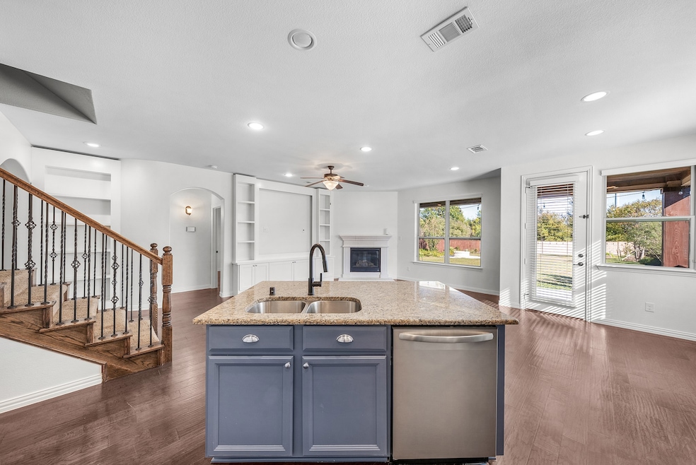 Kitchen featuring light stone counters, dishwasher, a glass covered fireplace, built in shelves, and dark wood-style floors