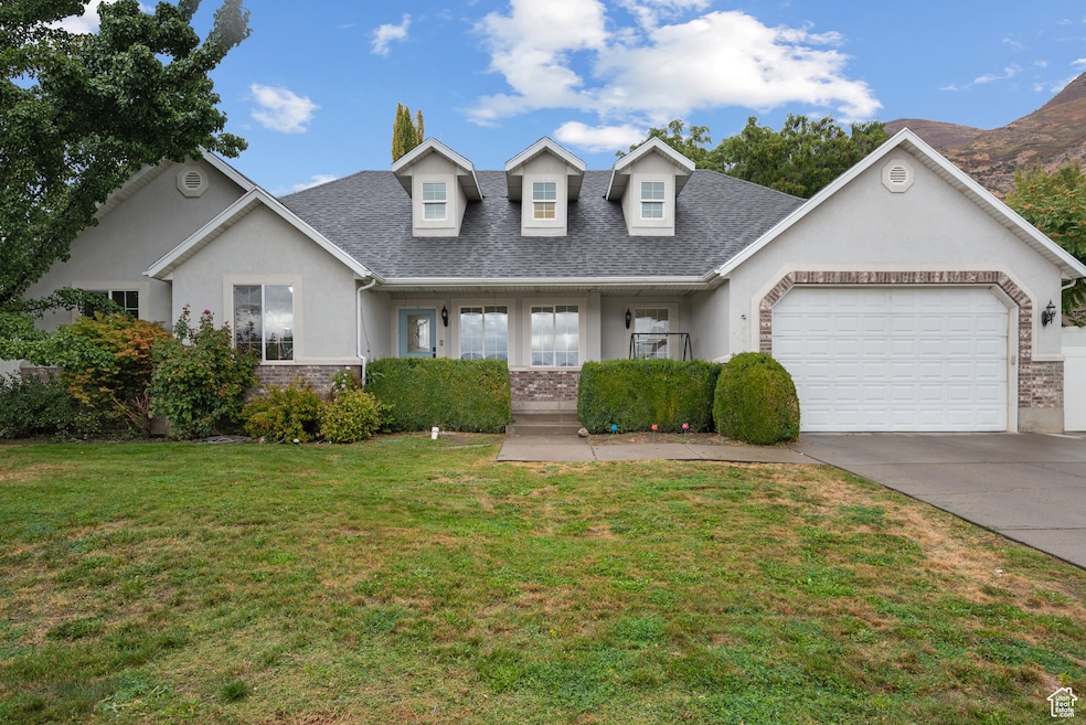 View of front of home with covered porch, stucco siding, a front lawn, driveway, and roof with shingles