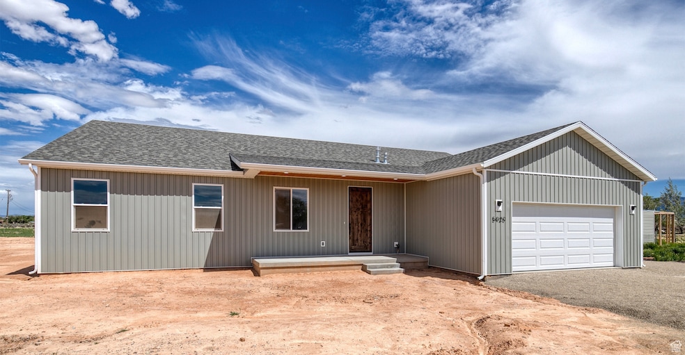 Ranch-style house featuring a shingled roof, an attached garage, dirt driveway, and a patio