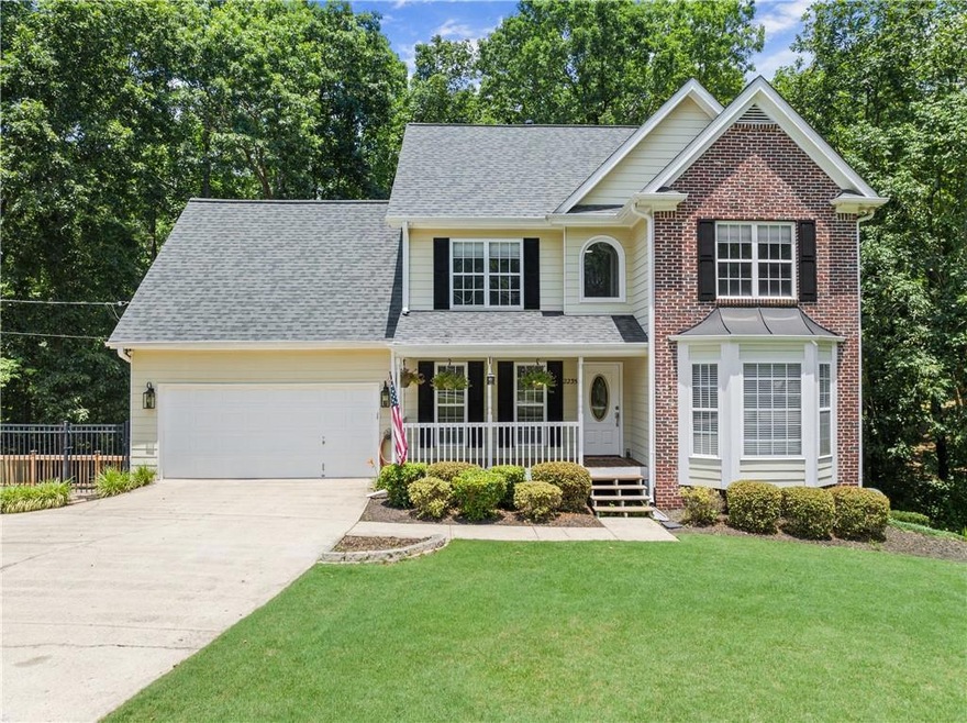 Traditional home with covered porch, a garage, driveway, a shingled roof, and brick siding