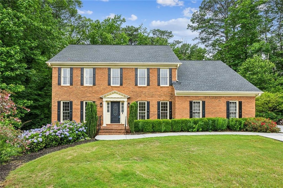 Colonial home with a front lawn, brick siding, and roof with shingles