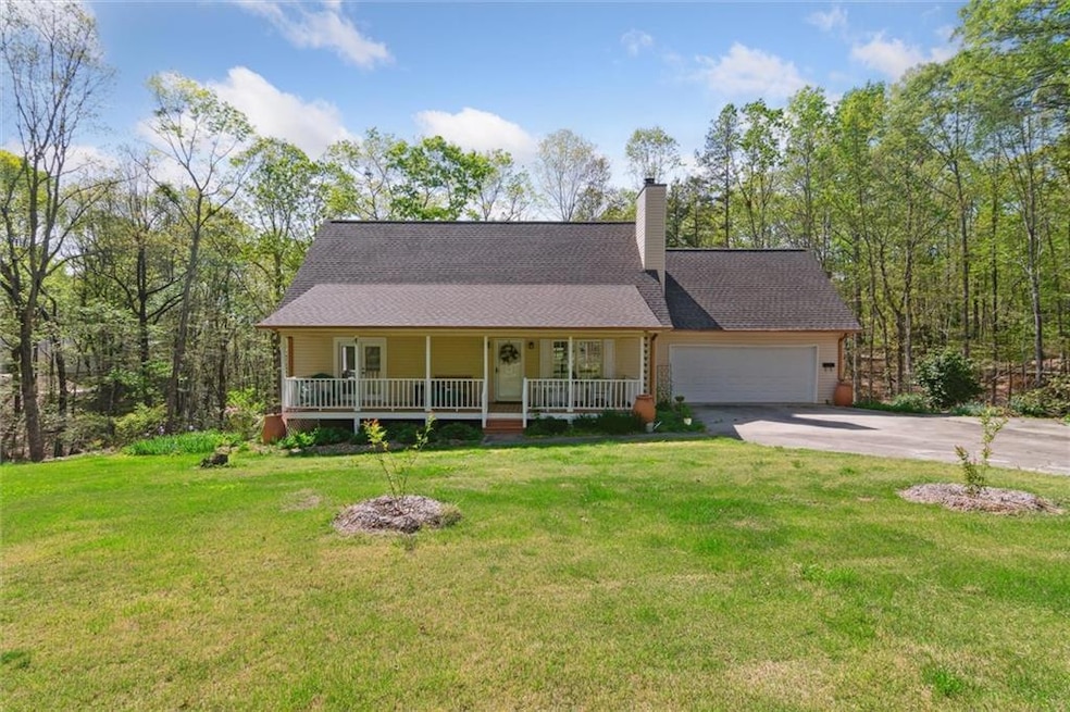 View of front of home with covered porch, concrete driveway, an attached garage, a front lawn, and a chimney