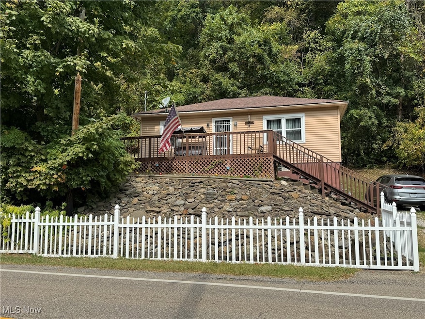View of front of house with stairway, a fenced front yard, a wooden deck, and a view of trees