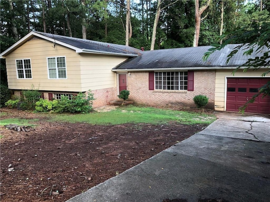 Split level home with an attached garage, brick siding, concrete driveway, and view of scattered trees