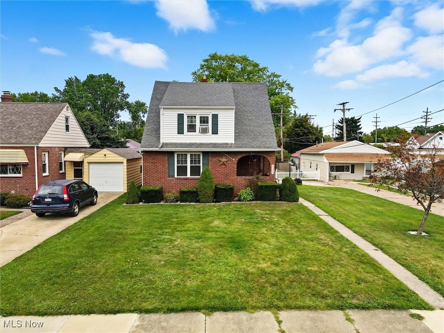 View of front facade featuring an outdoor structure, brick siding, roof with shingles, concrete driveway, and a front lawn