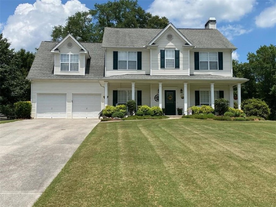 Colonial inspired home featuring concrete driveway, a chimney, a front yard, a shingled roof, and covered porch