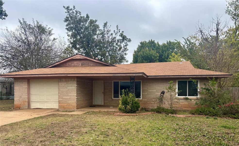 Single story home featuring a front lawn, driveway, an attached garage, brick siding, and a shingled roof