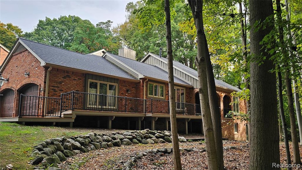 Rear view of house featuring a wooden deck, brick siding, a shingled roof, a chimney, and a garage