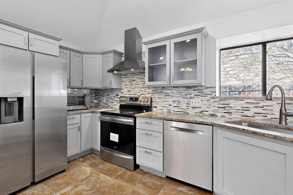 Kitchen with stainless steel appliances, gray cabinets, light stone countertops, ventilation hood, and glass insert cabinets