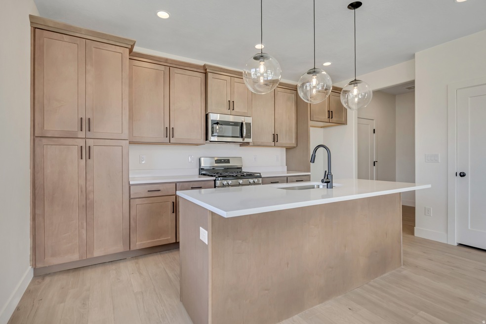 Kitchen featuring decorative light fixtures, appliances with stainless steel finishes, light wood-type flooring, a center island with sink, and recessed lighting